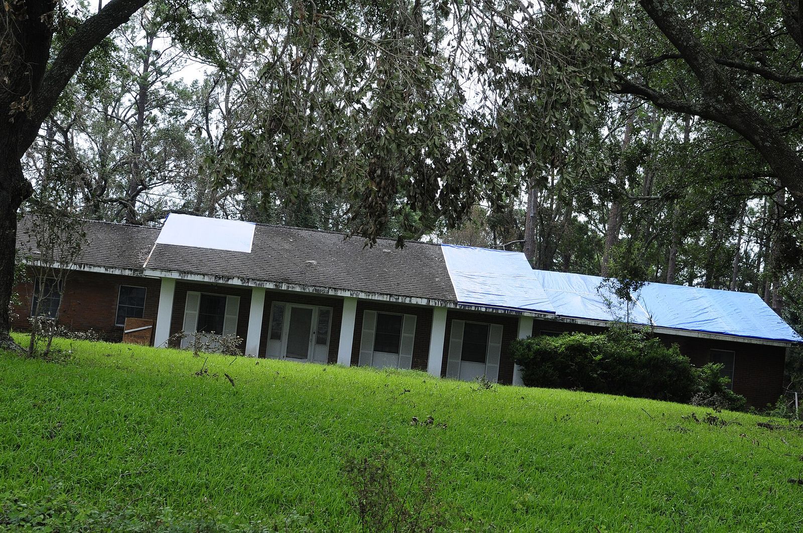 Storm-damaged house under a blue tarp, waiting on a roof replacement
