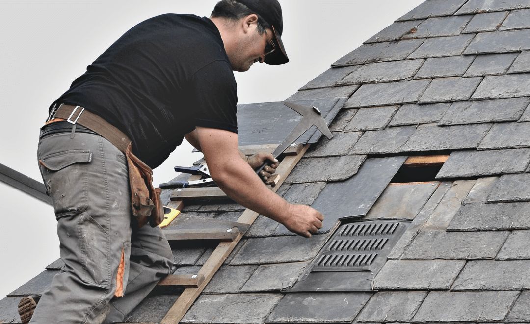 Roofer replacing a damaged section of shingles near the ridge